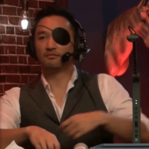 Un homme portant un gilet sans manches et un bandeau sur l'œil, utilisant des écouteurs et un micro, avec un fond décoratif en briques et des lumières tamisées.